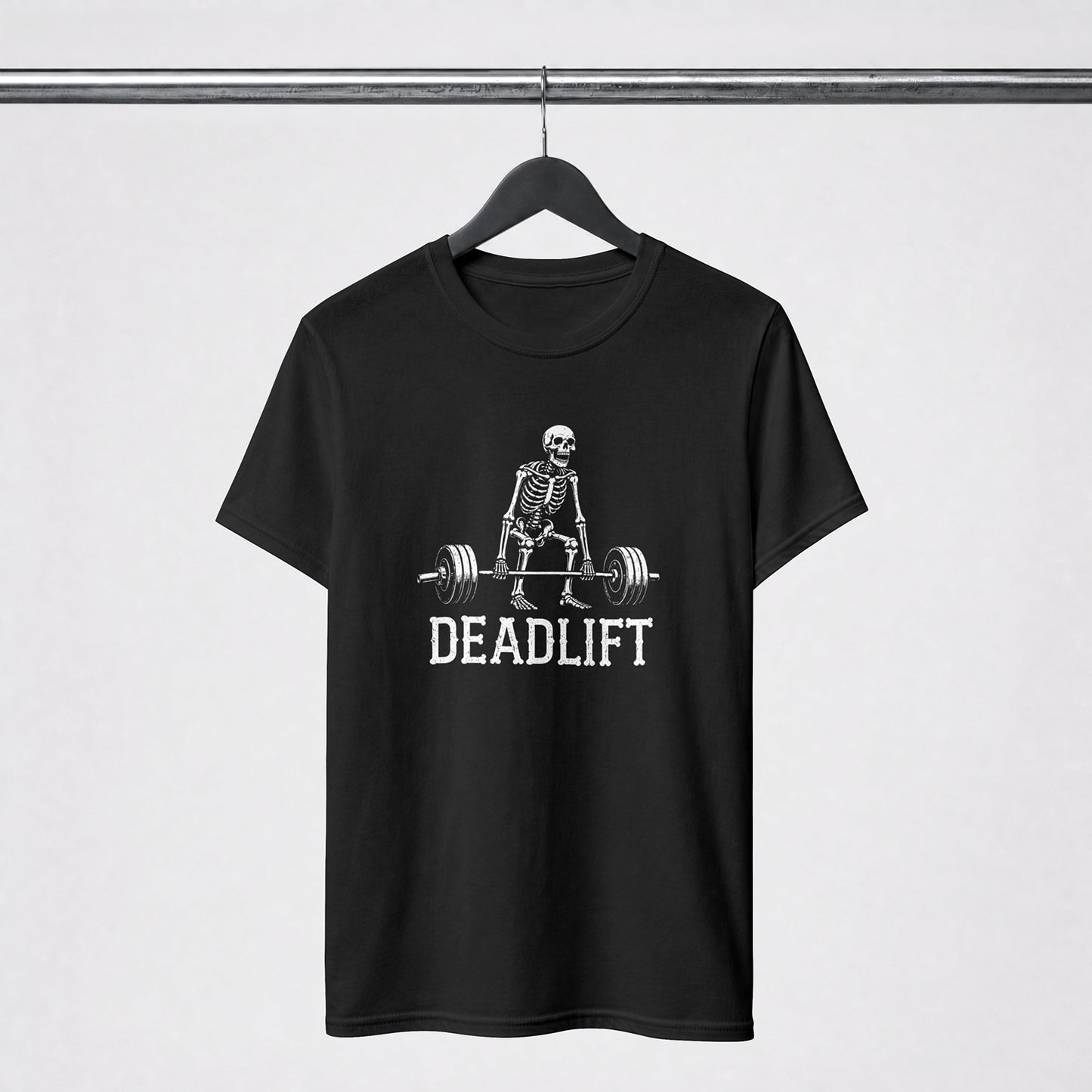 A black short-sleeve t-shirt hanging on a black hanger from a metal rack, featuring a white graphic of a skeleton lifting a barbell with the word 'DEADLIFT' printed below.