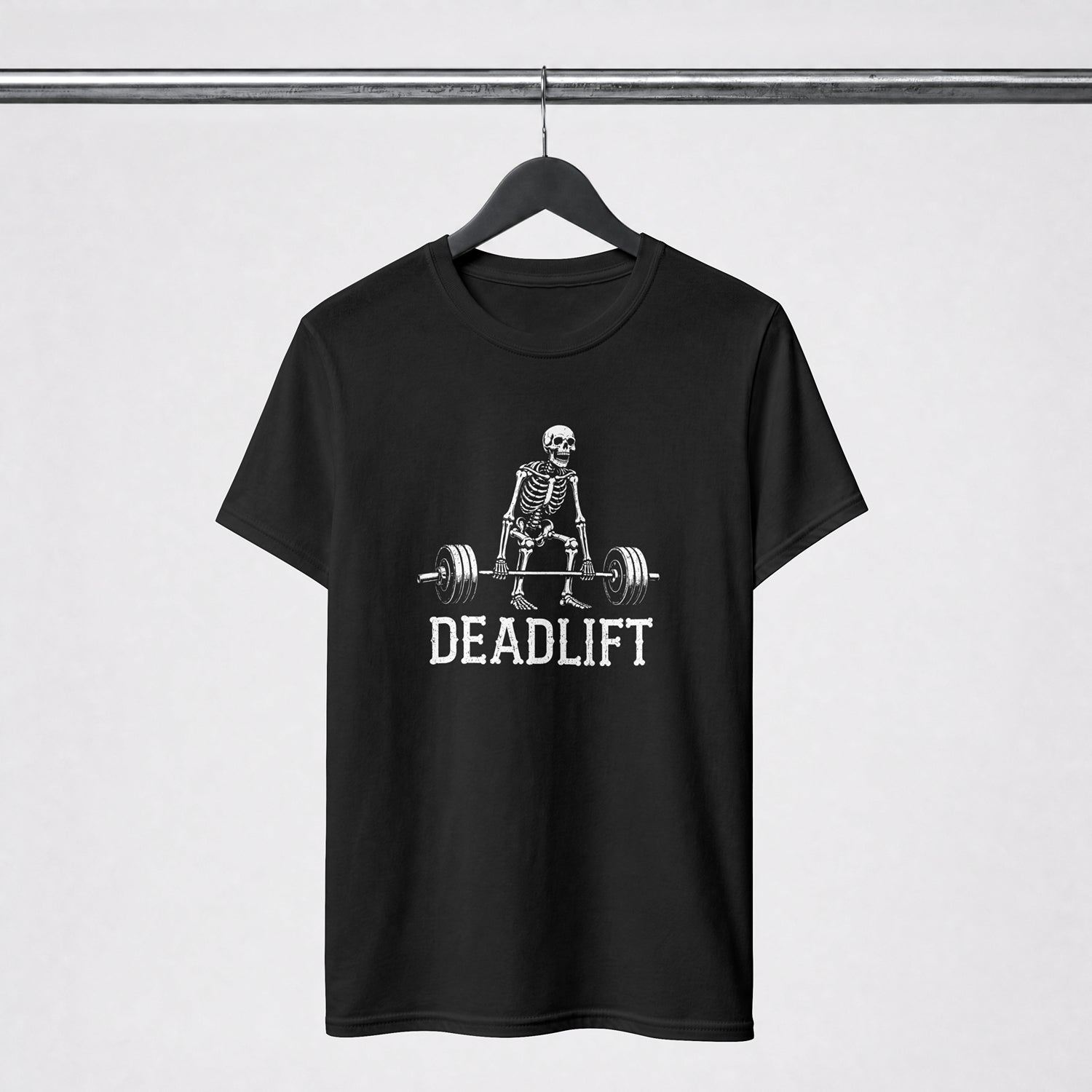 A black short-sleeve t-shirt hanging on a black hanger from a metal rack, featuring a white graphic of a skeleton lifting a barbell with the word 'DEADLIFT' printed below.
