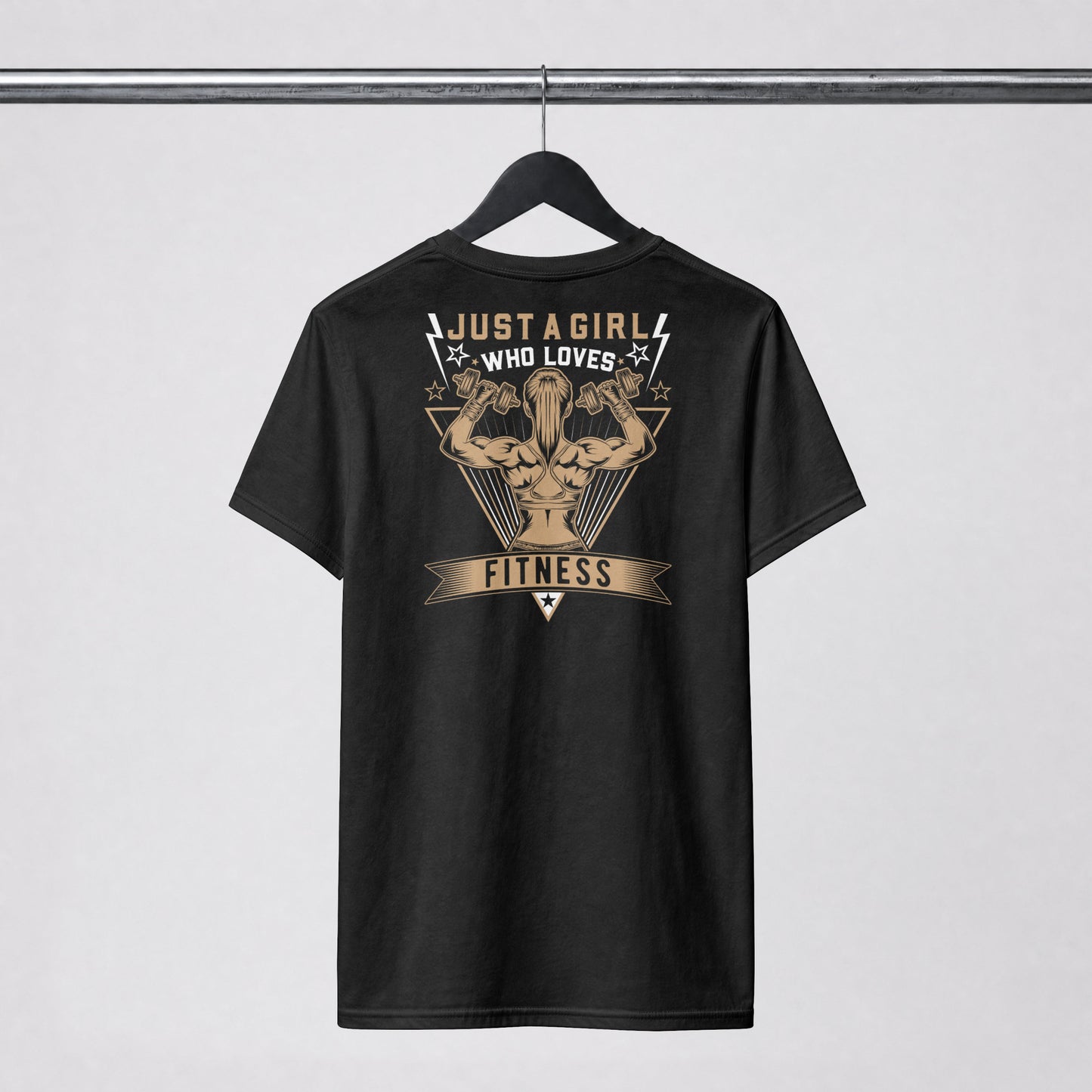 A black short-sleeve t-shirt hanging on a black hanger against a light gray background. The back of the shirt features a large graphic print in beige and white, showing a muscular flexing arm with the text 'JUST A GIRL WHO LOVES FITNESS'.