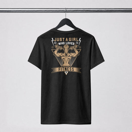 A black short-sleeve t-shirt hanging on a black hanger against a light gray background. The back of the shirt features a large graphic print in beige and white, showing a muscular flexing arm with the text 'JUST A GIRL WHO LOVES FITNESS'.